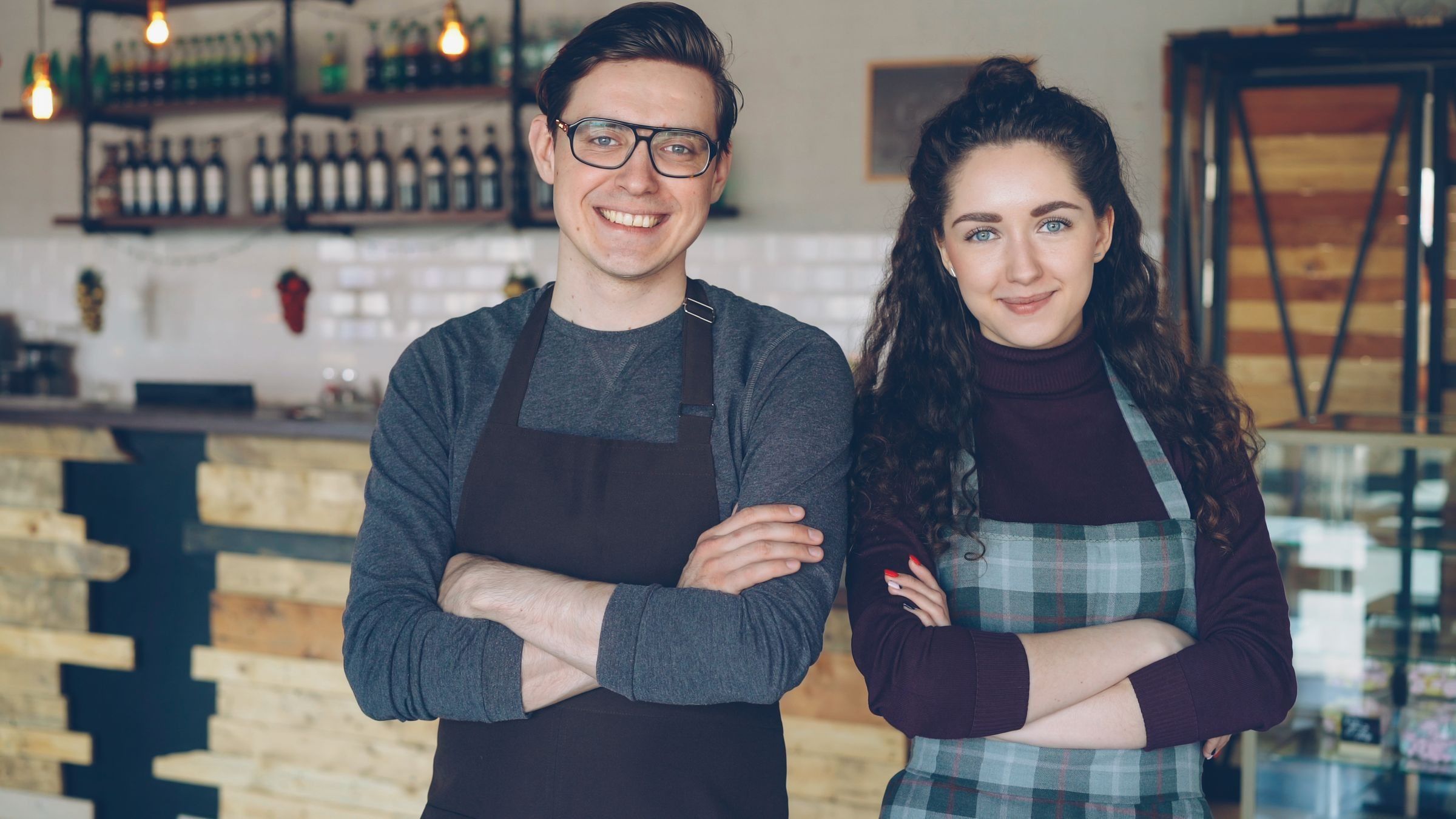 Two young café owners in aprons standing in their café