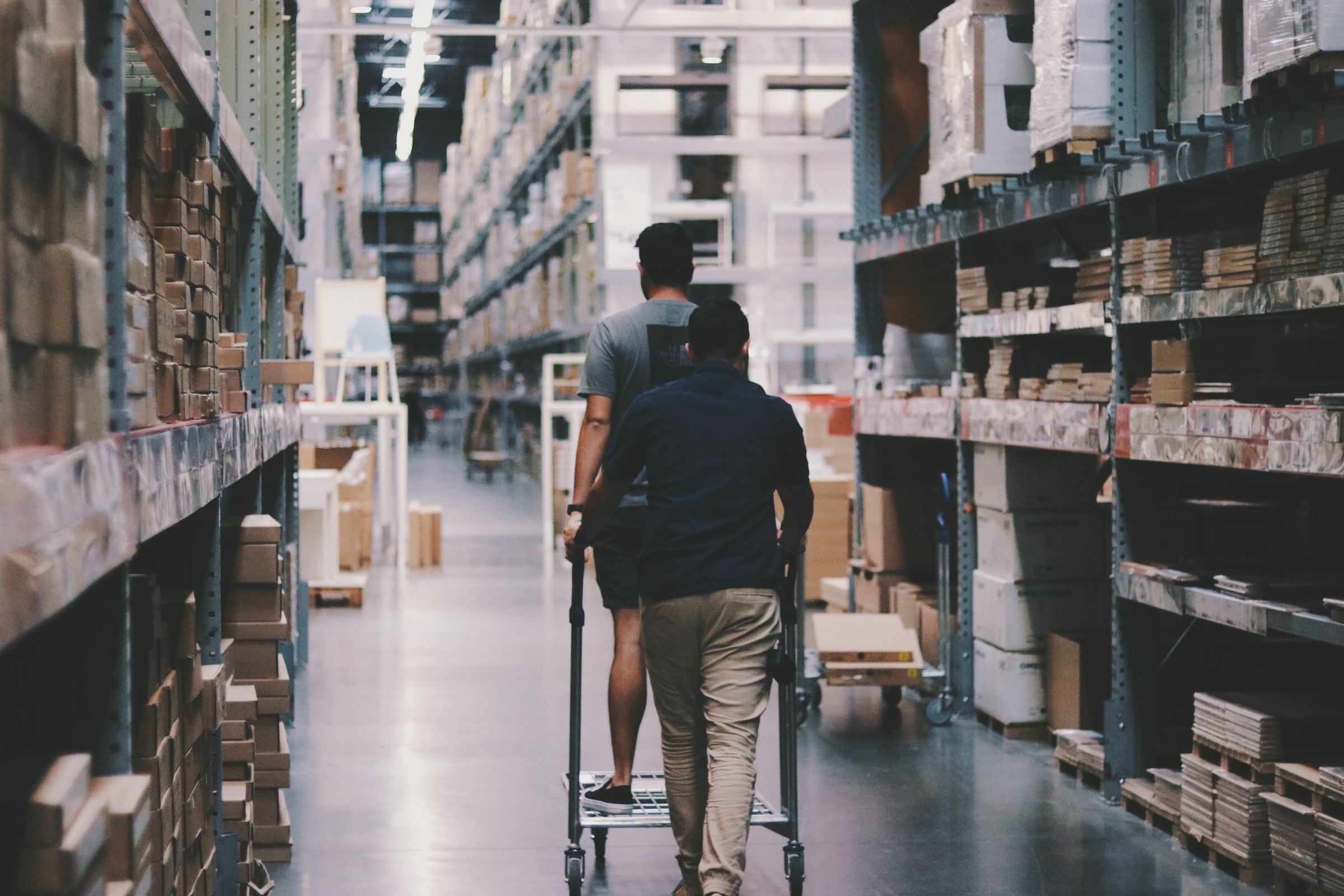 Two men moving a trolley through a large, dim warehouse