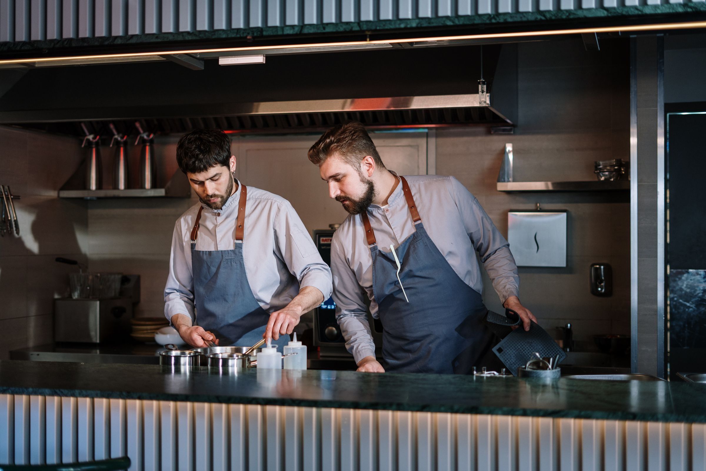 Two chefs cooking side by side in a dark, modern restaurant kitchen