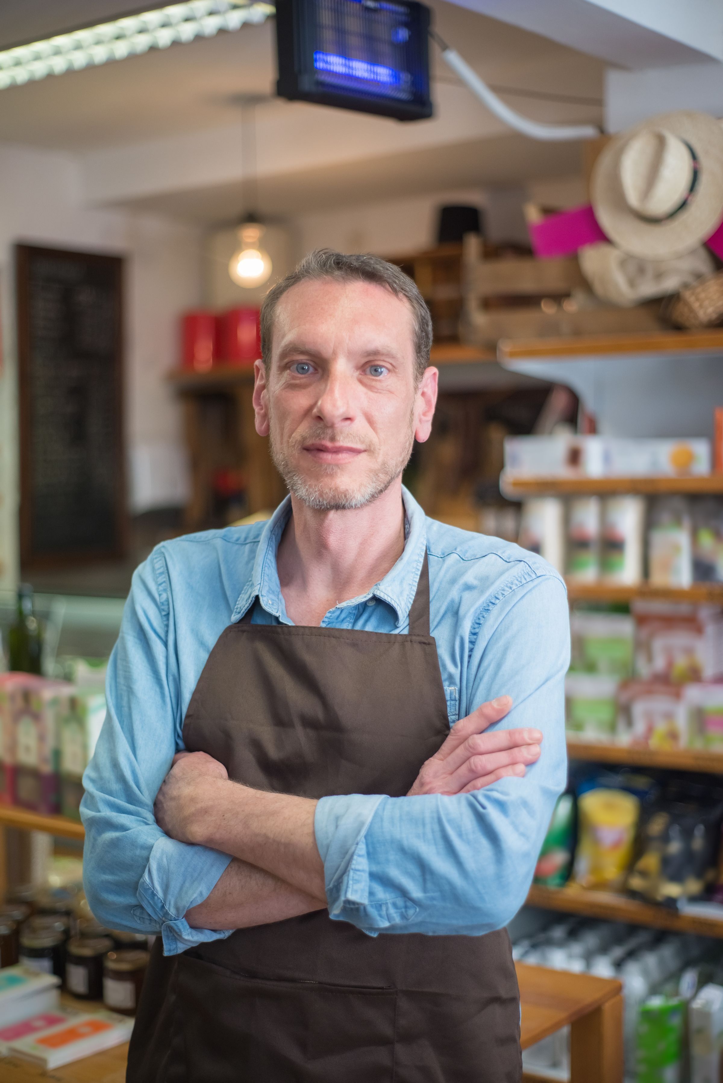 A shop owner with arms crossed in a small village store
